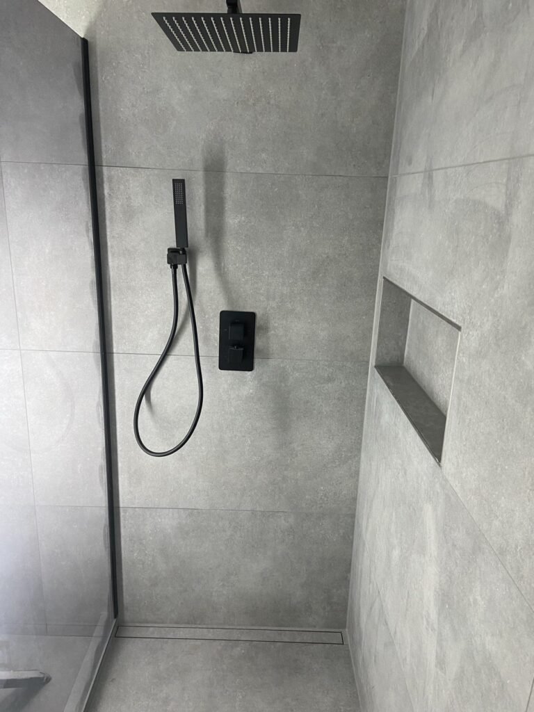 Dusche mit schwarzen Armaturen und grauen Großformatfliesen