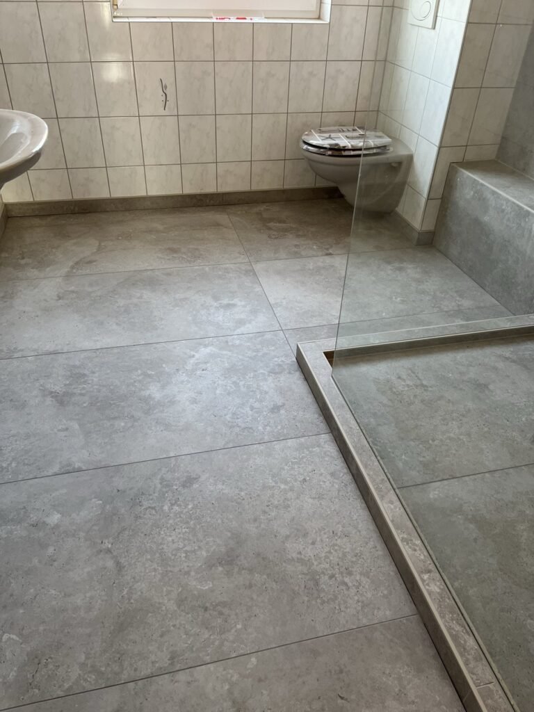 Gefliester Duschboden und graue Wandflächen