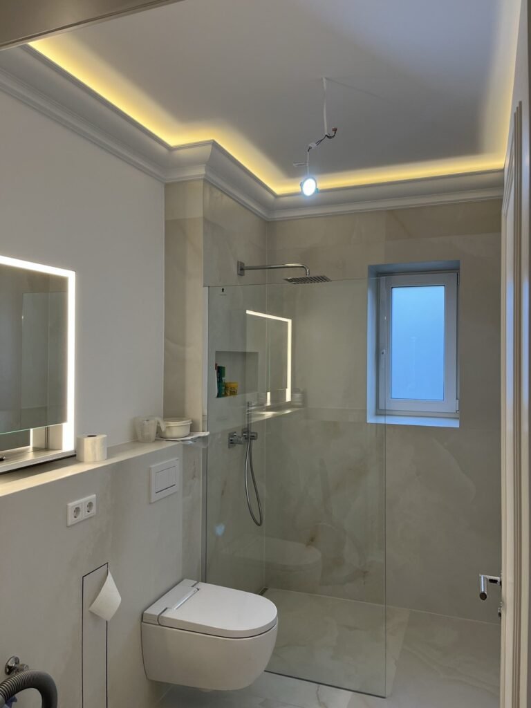 Helles Bad mit bodengleicher Dusche, Großformatfliesen und indirektem Deckenlicht
