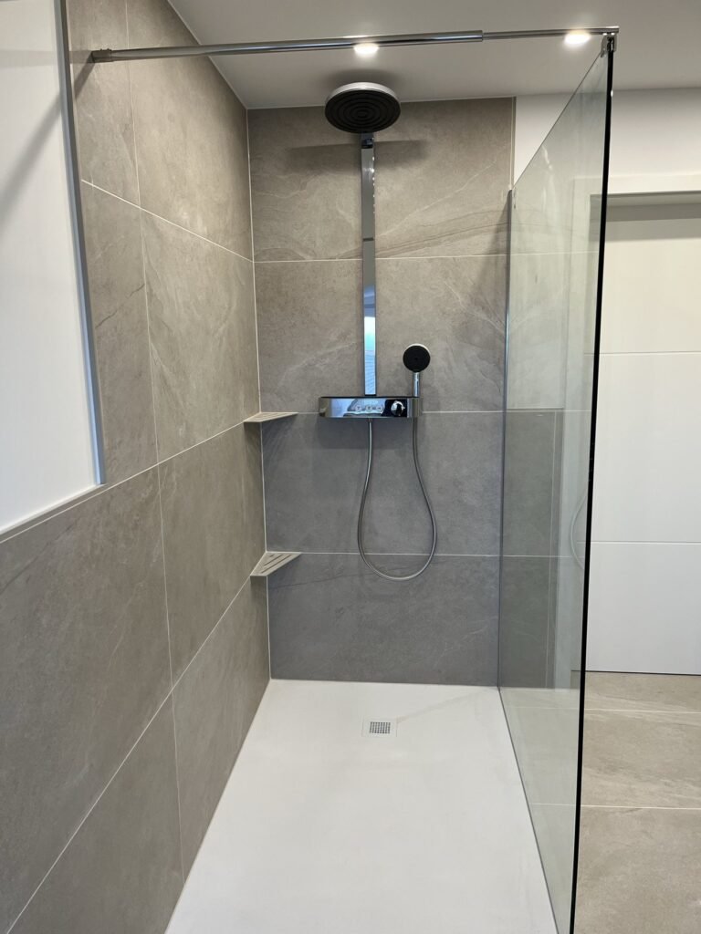 Dusche mit Glasabtrennung und grauen Fliesen