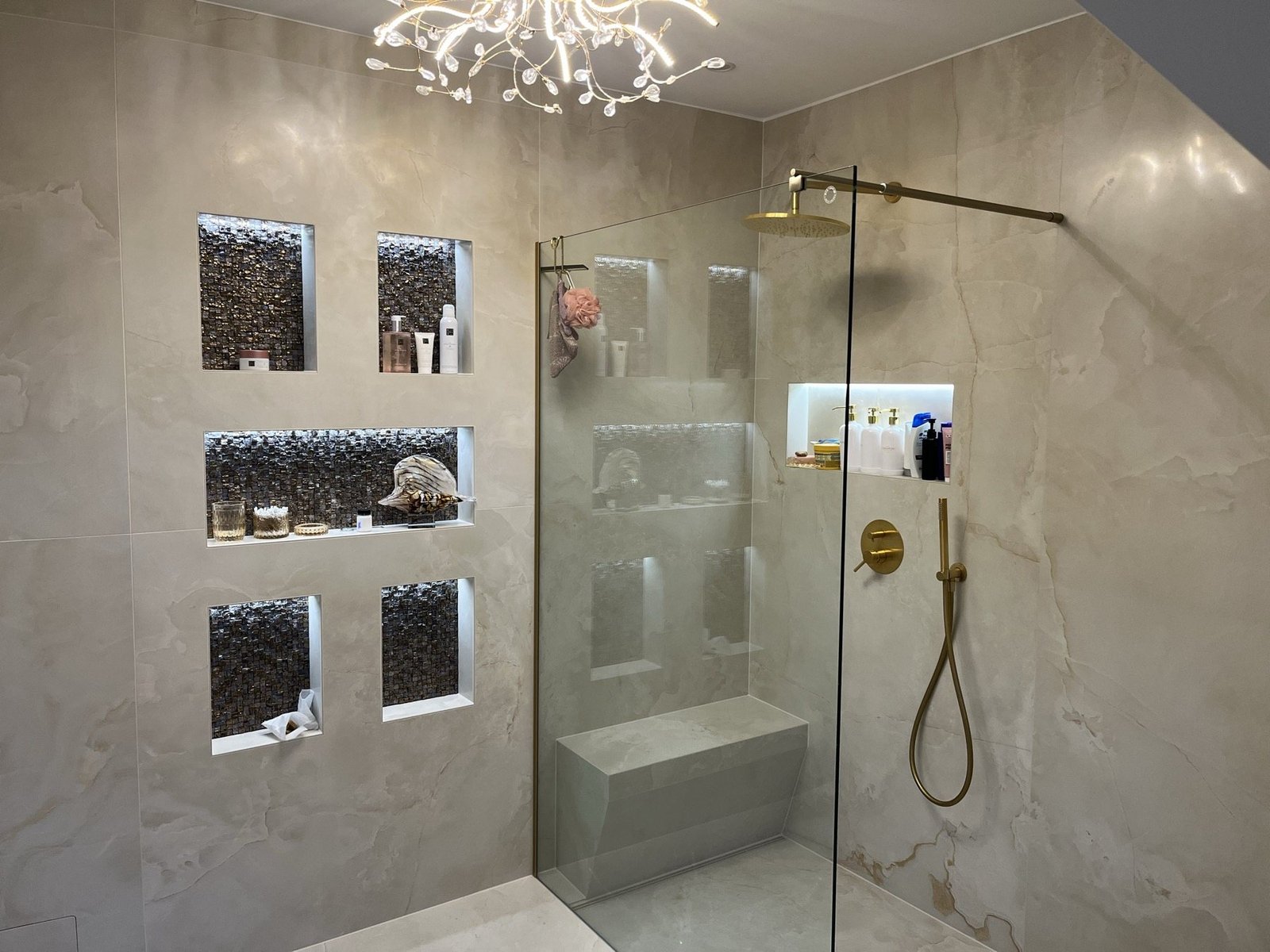 Dusche mit beleuchteten Mosaiknischen und goldfarbenen Armaturen